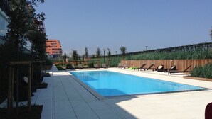 Una piscina rectangular con un borde de baldosas, rodeada de sillas de descanso y una valla de madera.