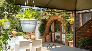 An outdoor patio area with wicker furniture, terracotta planters, and hanging plants.