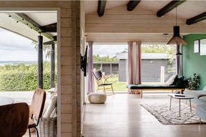 Un vaste espace de vie doté d’un plancher en bois, d’un canapé, d’un fauteuil, d’une petite table et d’un luminaire suspendu.