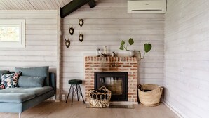 Una sala de estar acogedora con chimenea de ladrillo, un sofá y un taburete verde.
