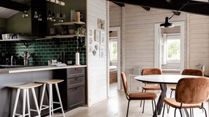 Una cocina moderna con salpicadero verde, estantes de madera e iluminación colgante. Hay un comedor con una mesa redonda y cuatro sillas.