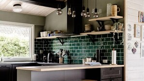 Una cocina moderna con una isla oscura, taburetes blancos y un salpicadero verde.