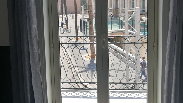 Vista a través de una ventana con cortinas, mostrando un edificio de varios pisos y una palmera en primer plano.