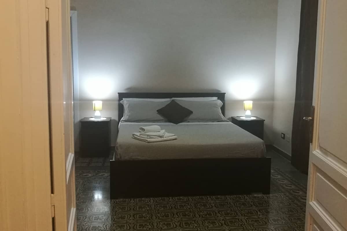 Ein Schlafzimmer mit einem Bett, zwei Nachttischlampen, einem gemusterten Boden und einer Tür links.