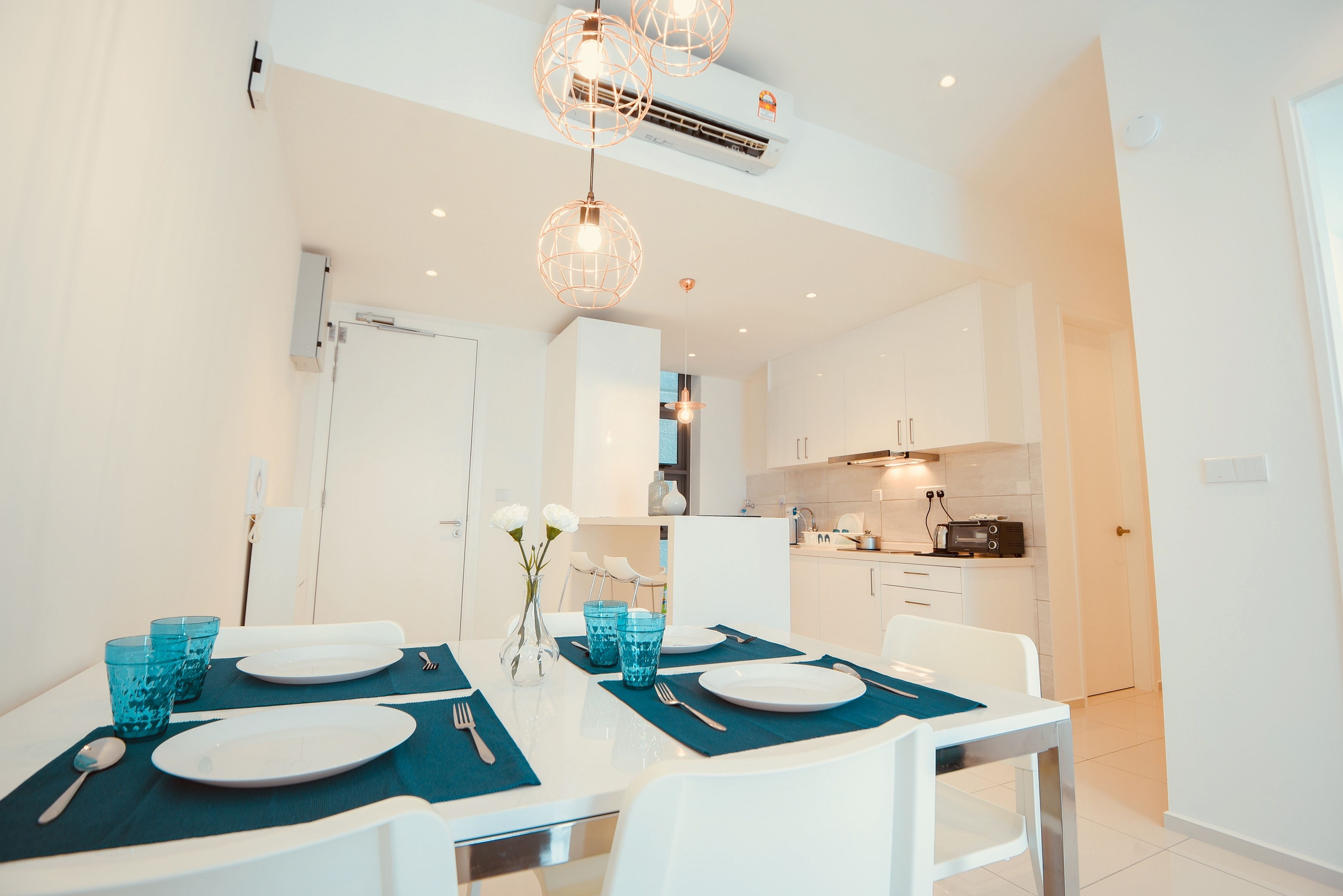 A modern dining area with a white table set for four, blue placemats, and a vase with flowers.