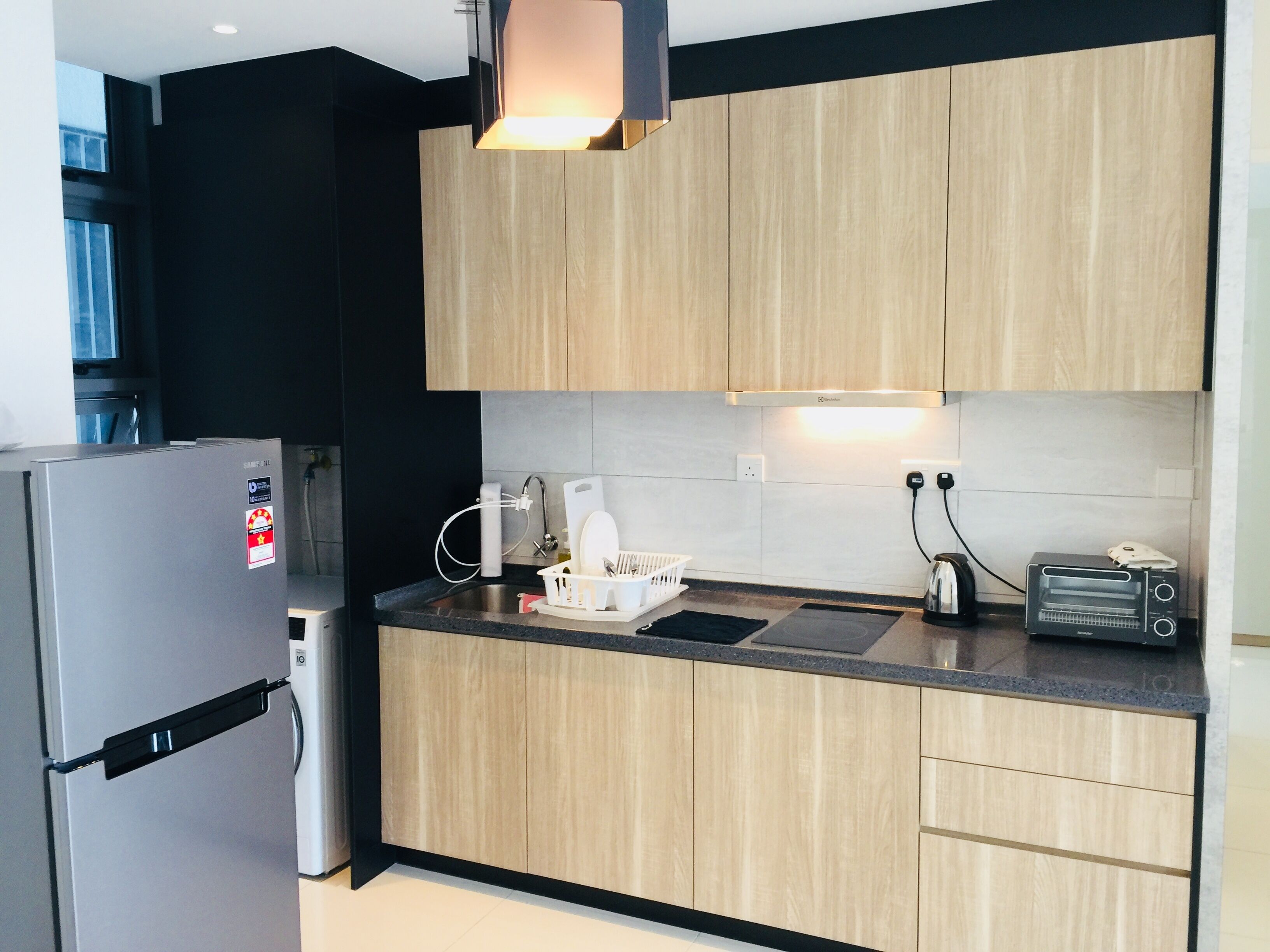A modern kitchen with wooden cabinets, a stainless steel refrigerator, a toaster, and a kettle.