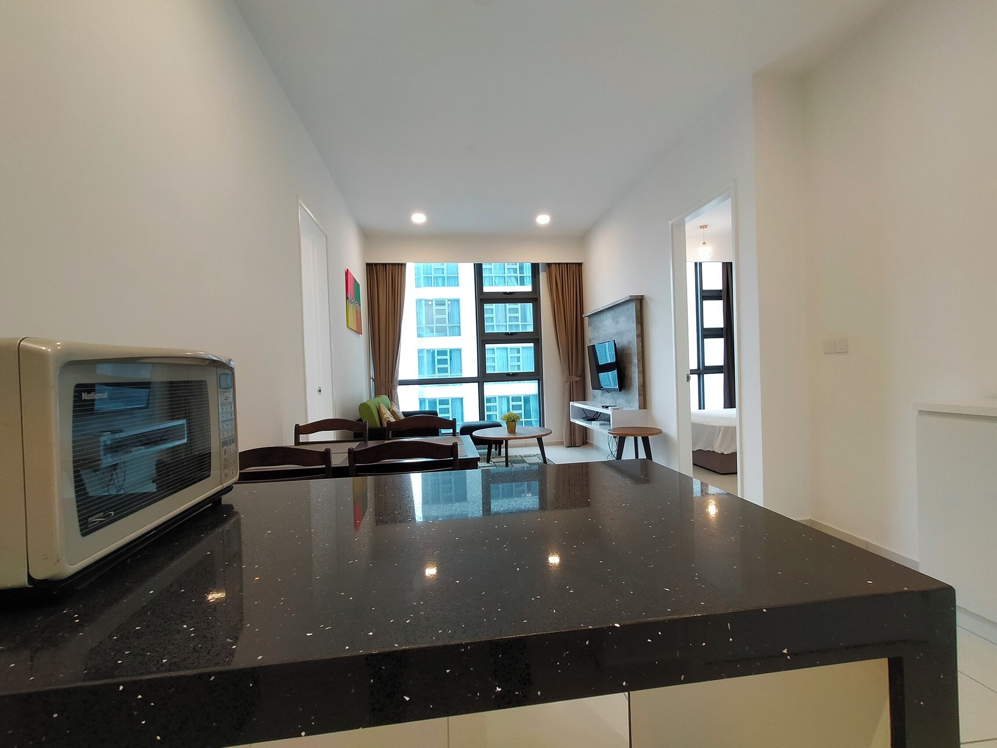 Una cocina moderna con encimera negra, microondas y comedor con sillas y mesa.