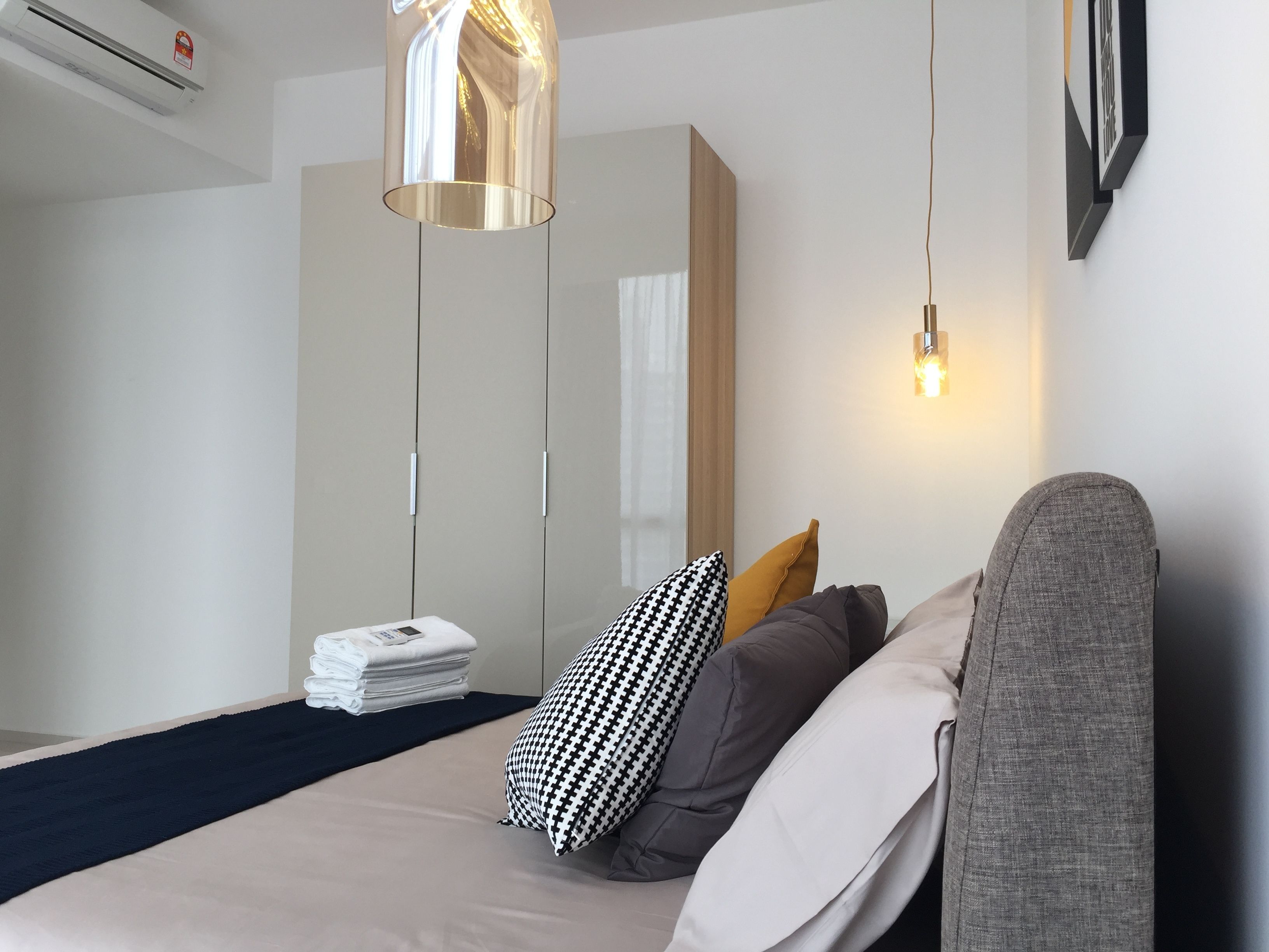 A modern bedroom with a bed, bedside tables, a hanging light fixture, and a wardrobe.