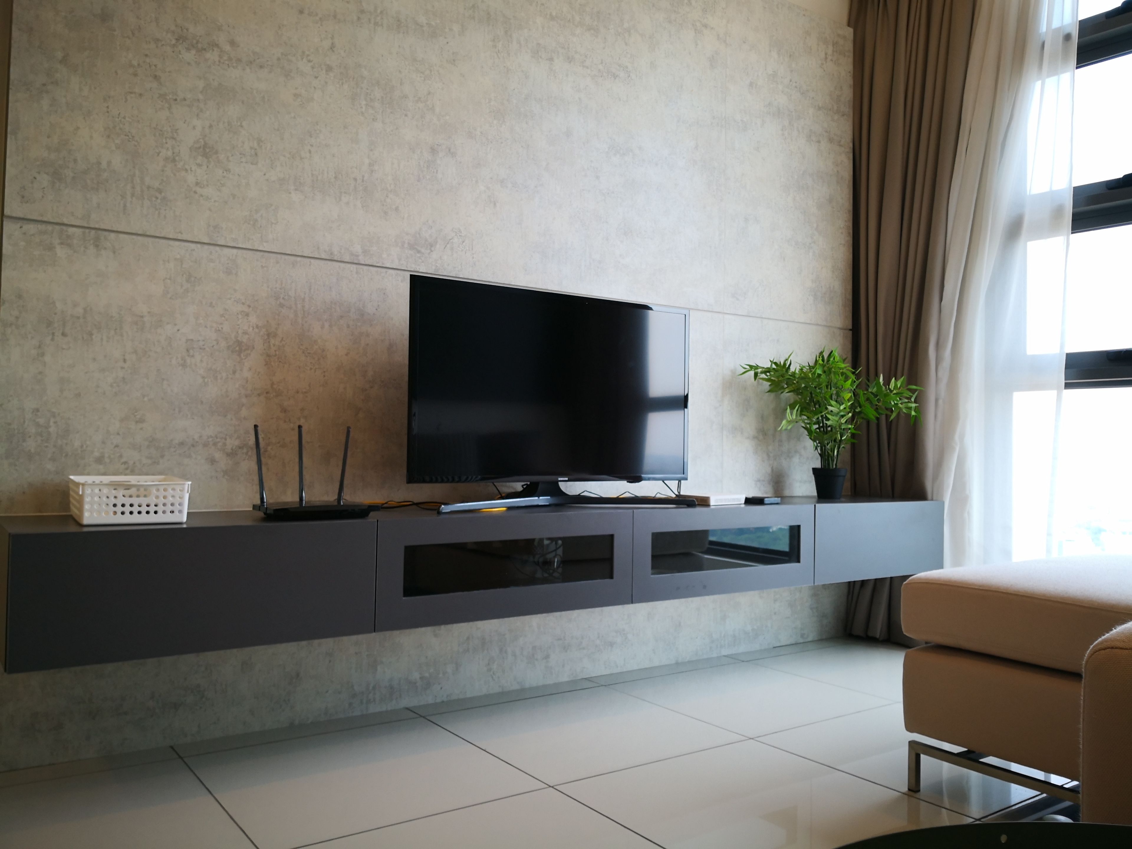 A modern living room with a flat-screen TV on a dark console, a potted plant, and a beige sofa.