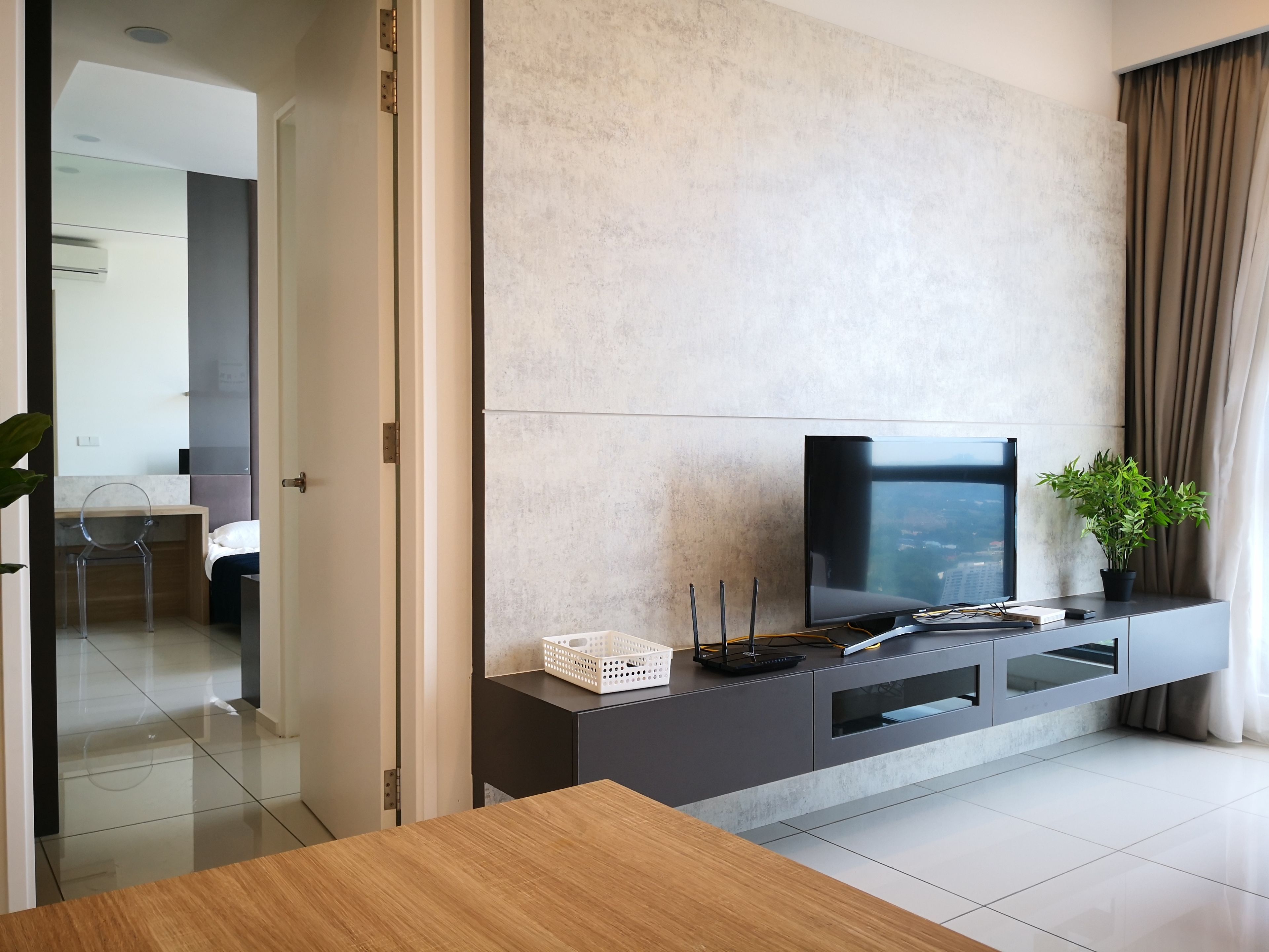 A modern living room with a flat-screen TV on a dark console, a potted plant, and a wooden table.