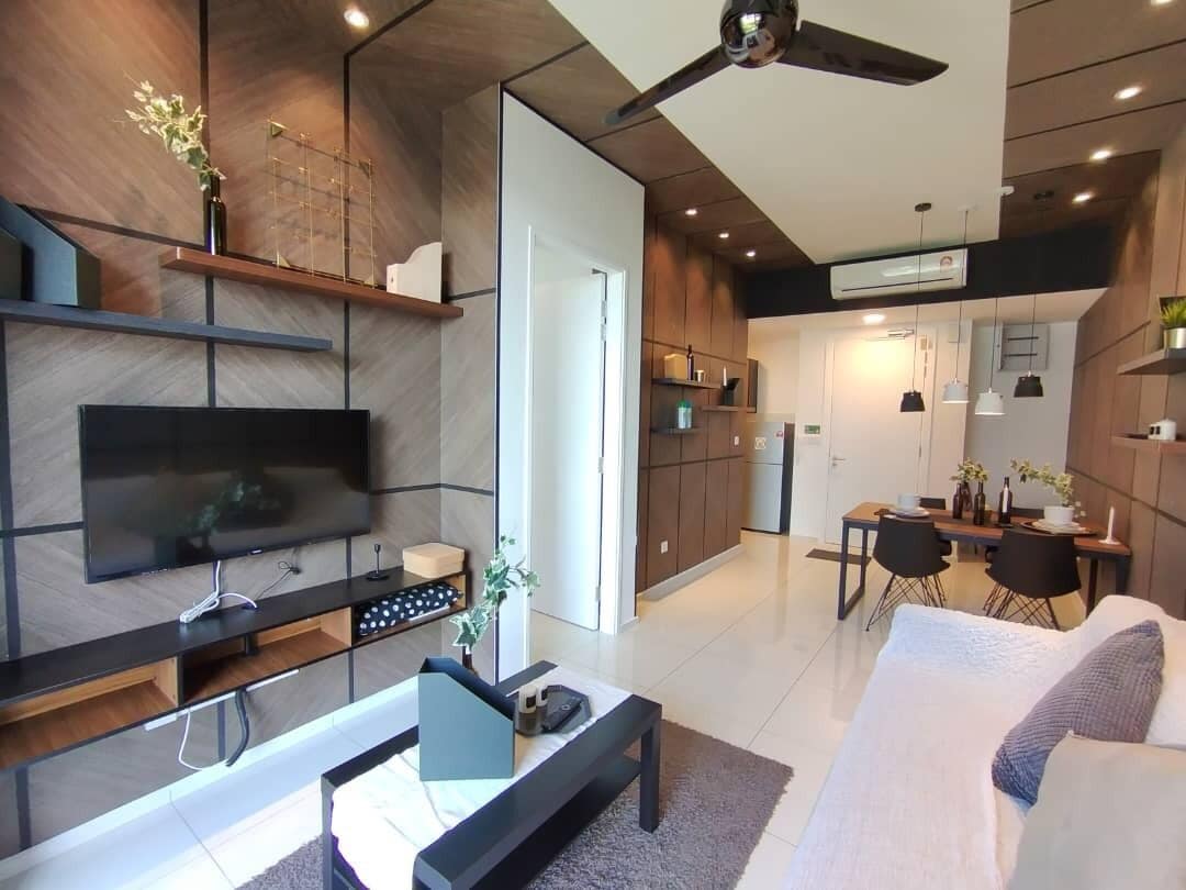 A modern living room with a flat-screen TV, a coffee table, and a sofa. There is a dining area with a table and chairs, and a kitchen in the background.