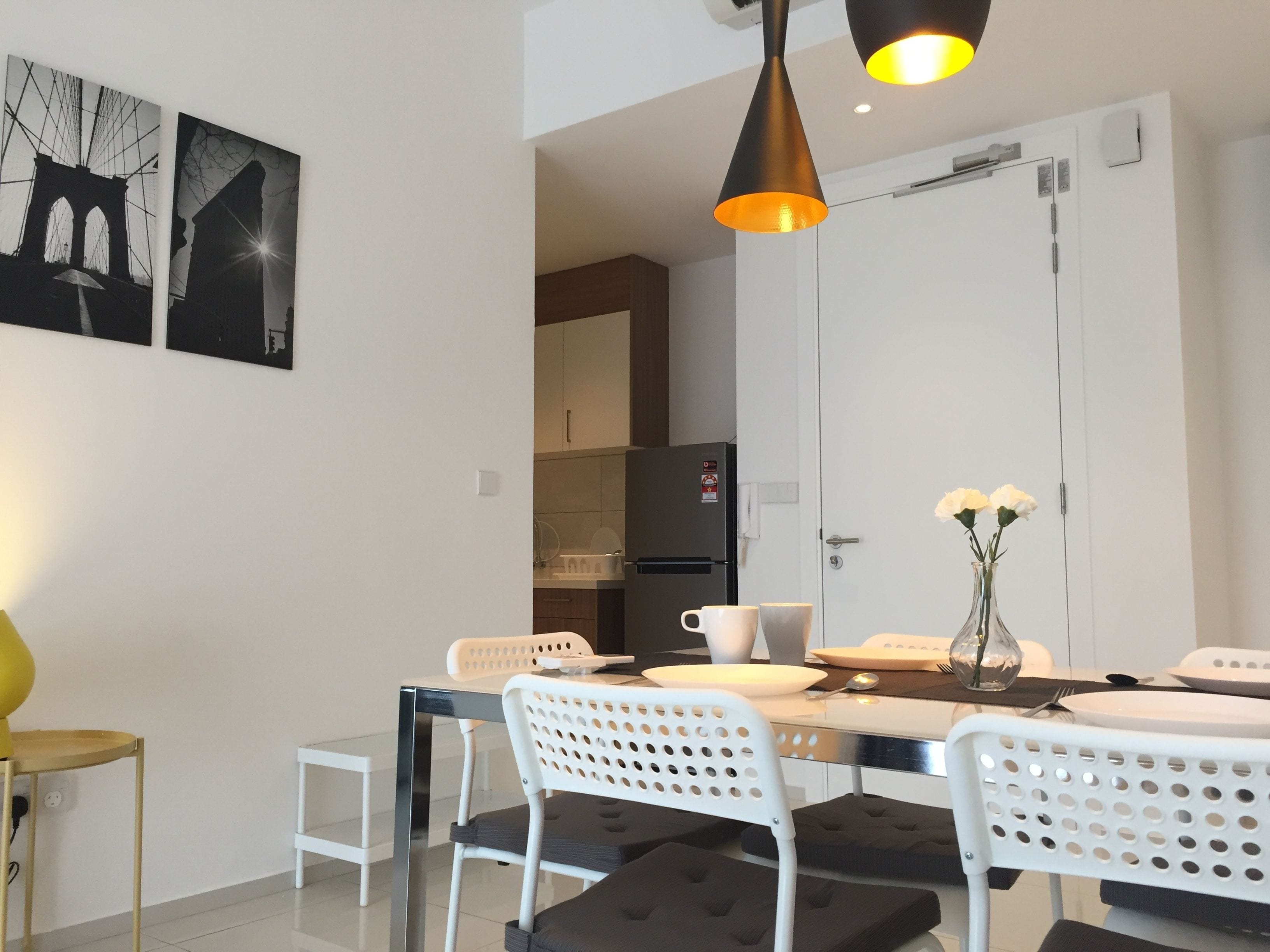 A modern dining area with a white table, black cushioned chairs, and a black pendant light.