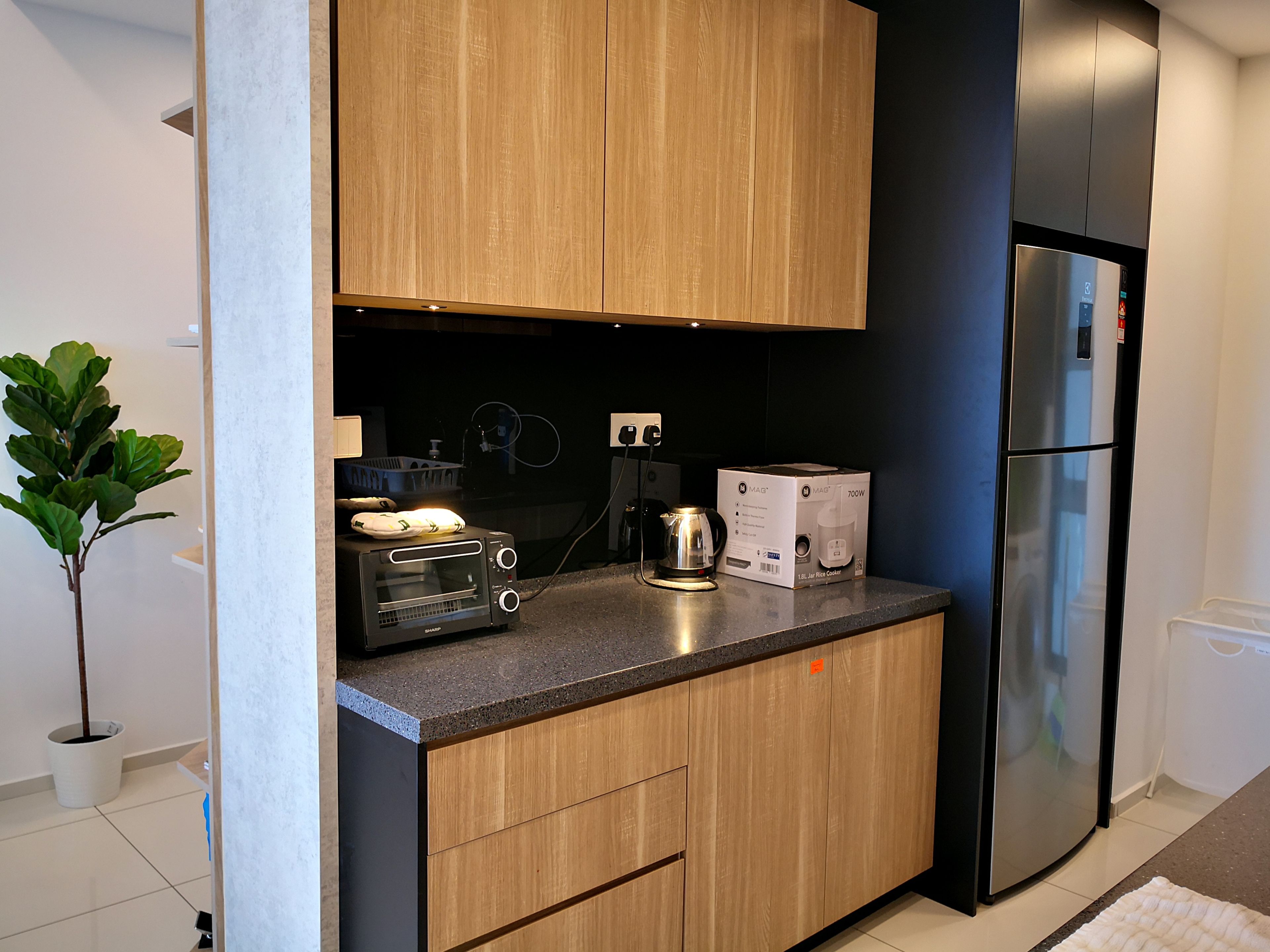 A modern kitchen with wooden cabinets, a stainless steel refrigerator, a toaster, and a rice cooker on the counter.