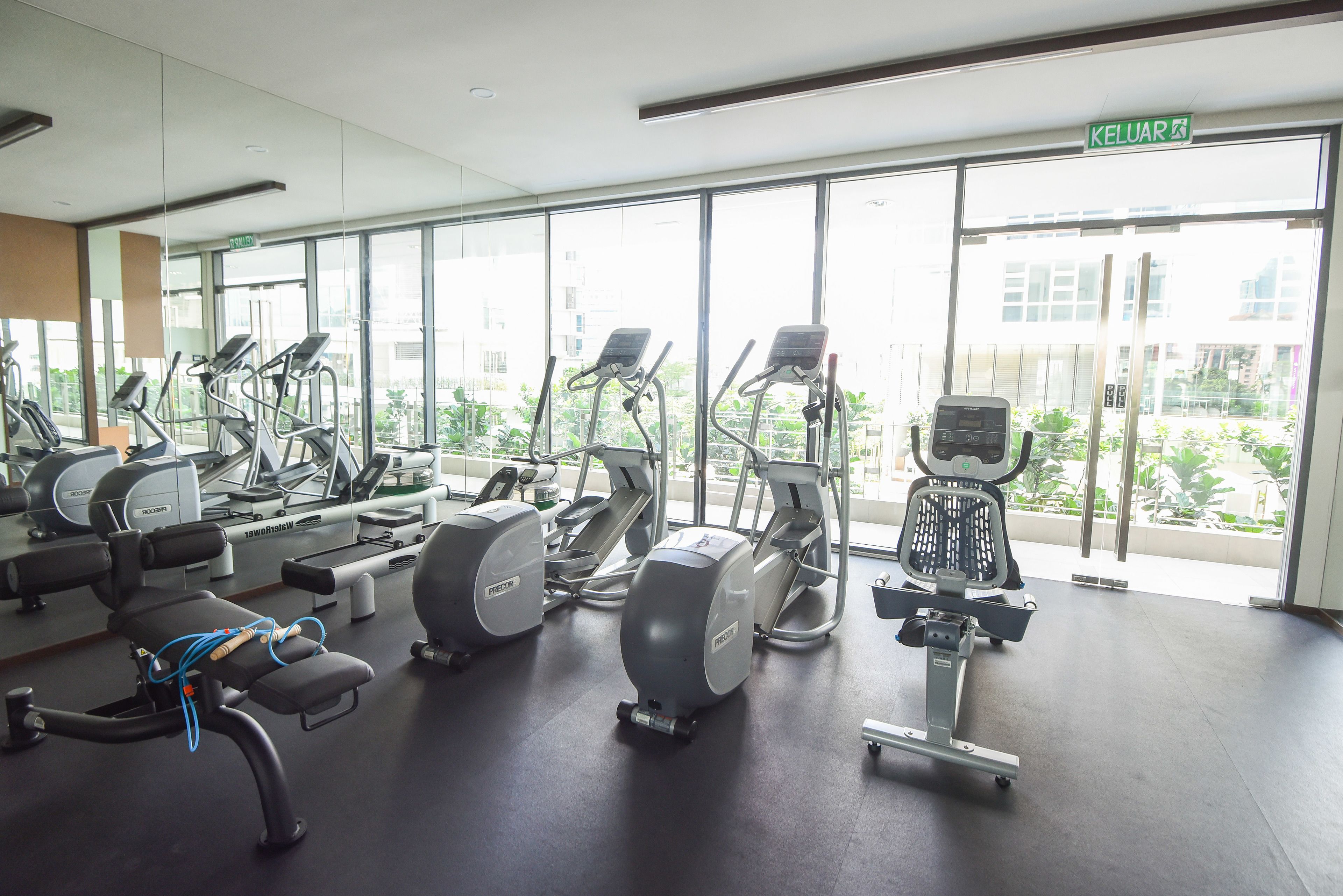 A gym with various exercise machines, large windows, and a clear view of the outside.
