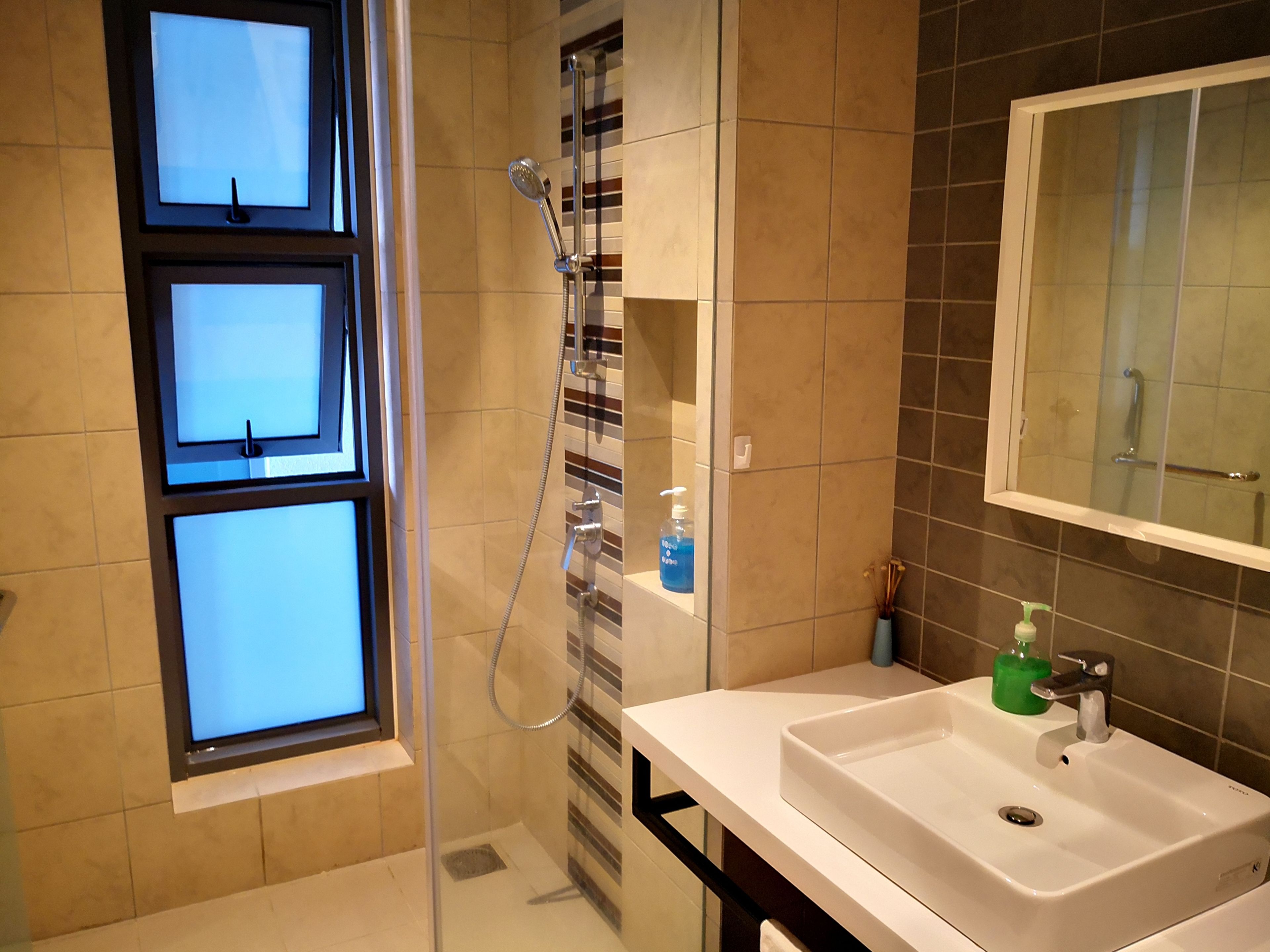 Un baño moderno con ducha de vidrio, un lavamanos blanco y un espejo encima.