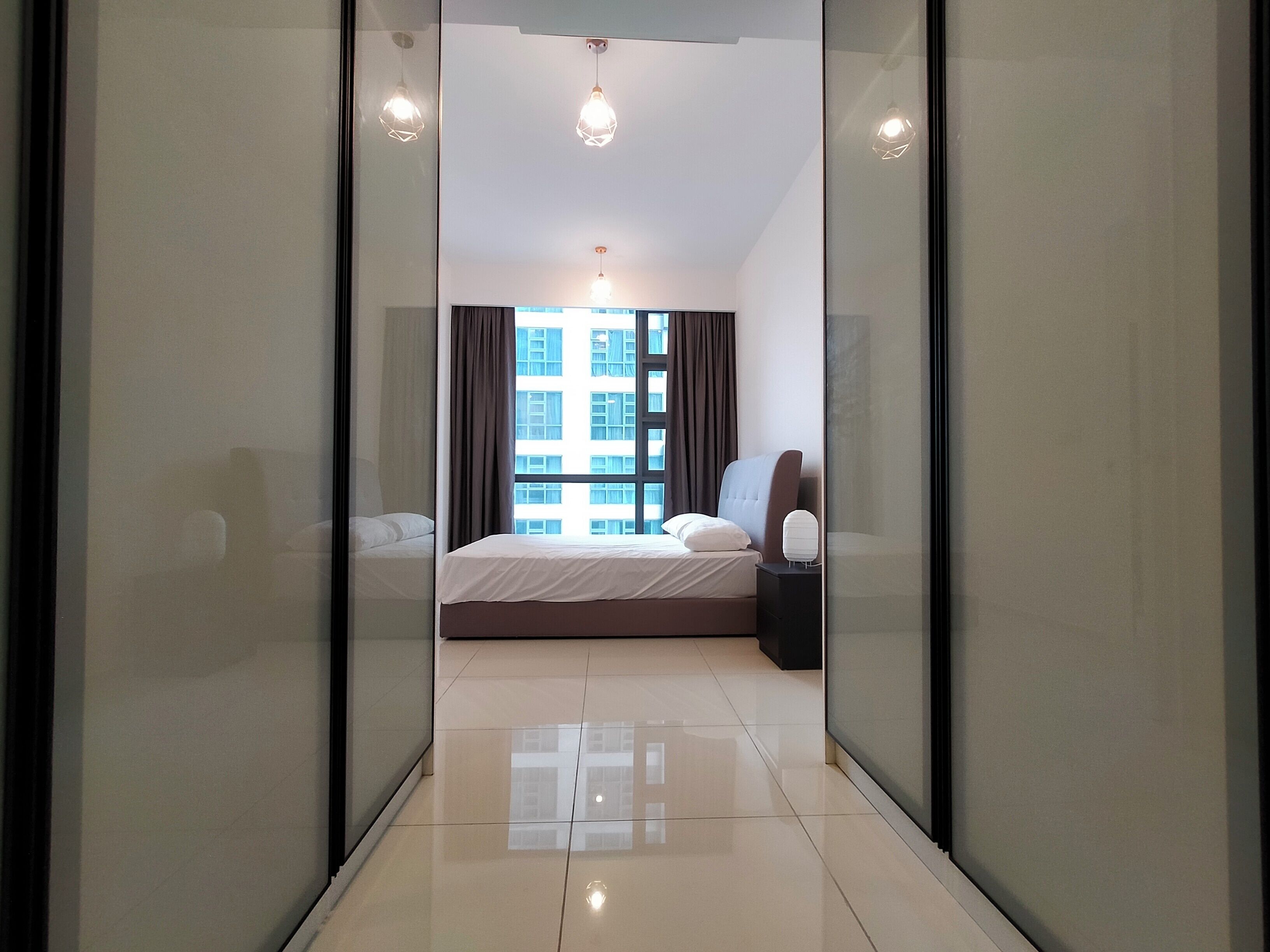 Una habitación de hotel moderna con una cama, una mesita de noche, una lámpara y vistas a un edificio a través del ventanal.