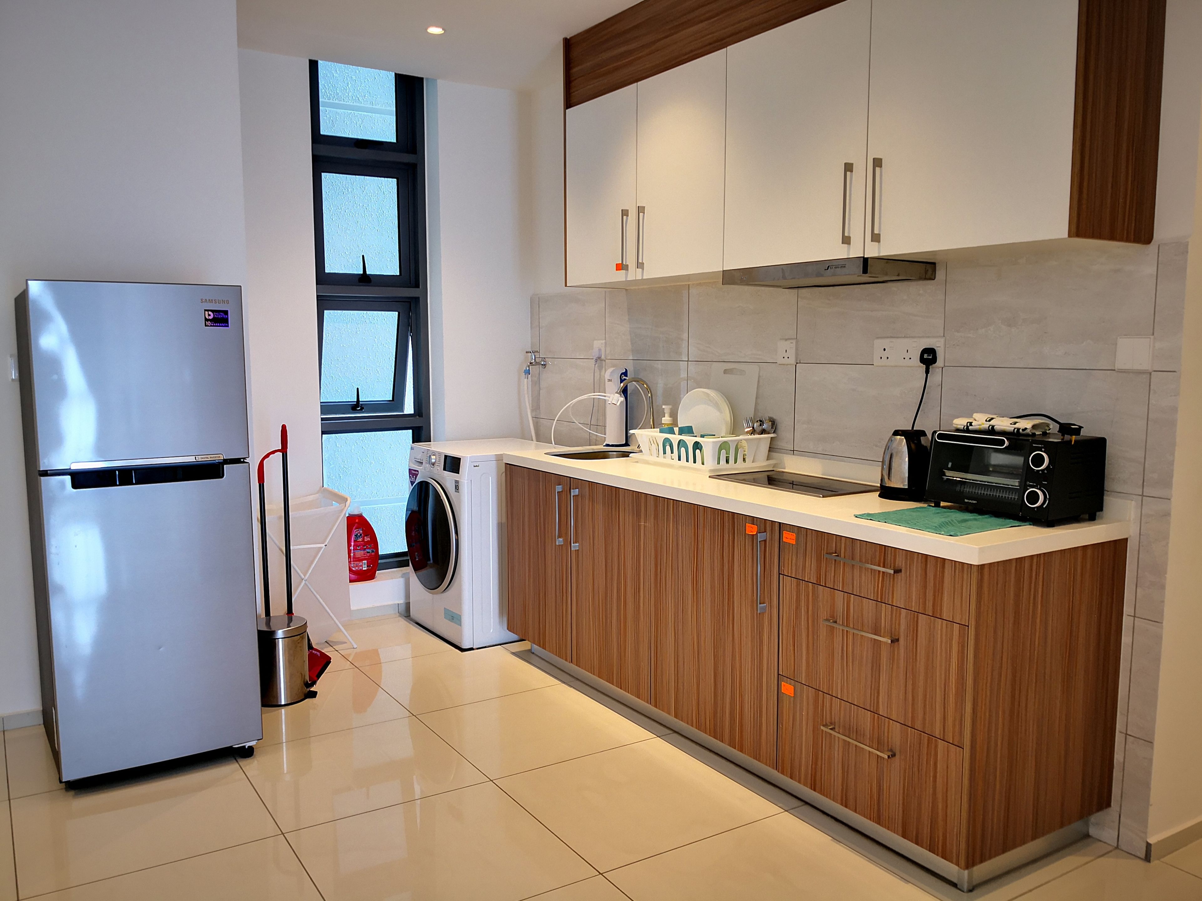 Una cocina moderna con un refrigerador de acero inoxidable, lavadora, armarios de madera, un lavamanos y un tostador.