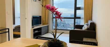 Una sala de estar moderna con un ventanal grande, un televisor de pantalla plana, un sofá y una mesa de comedor con un centro de mesa decorativo con una orquídea.