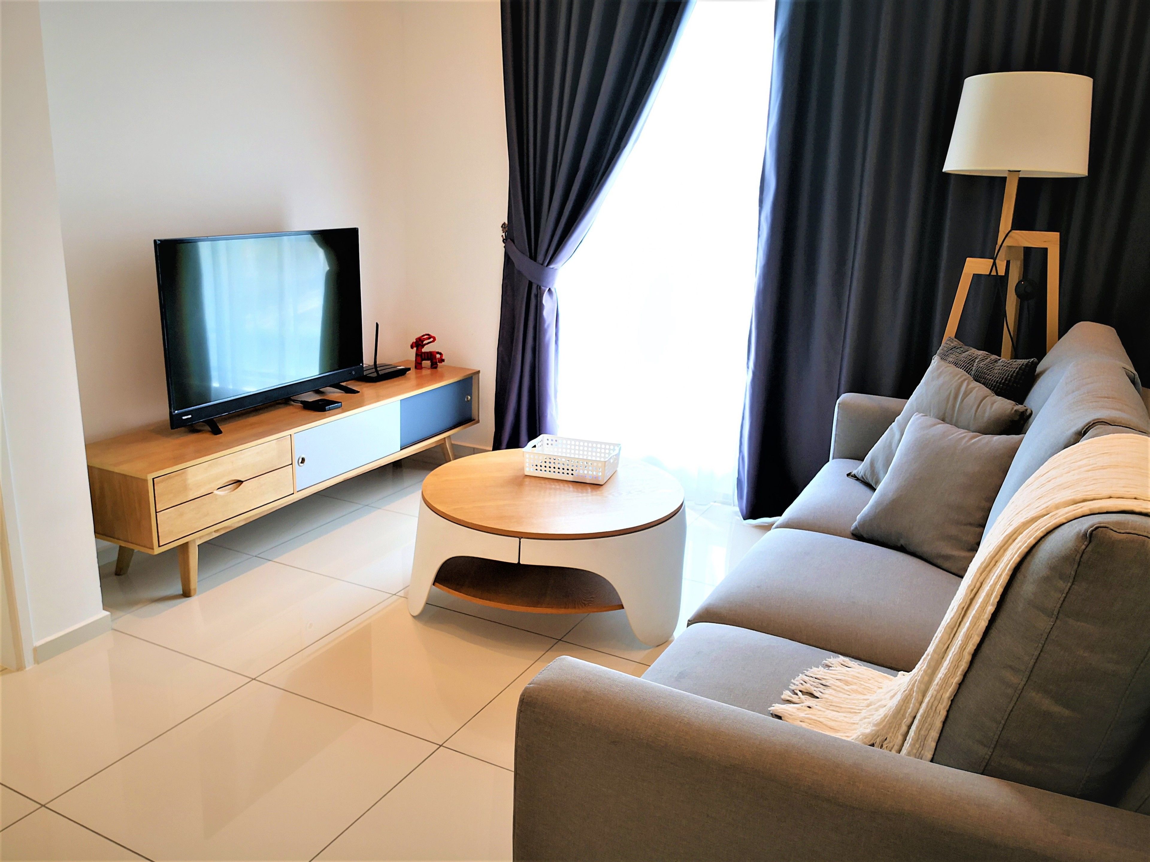 A modern living room with a flat-screen TV, a wooden coffee table, a sofa, and a lamp.