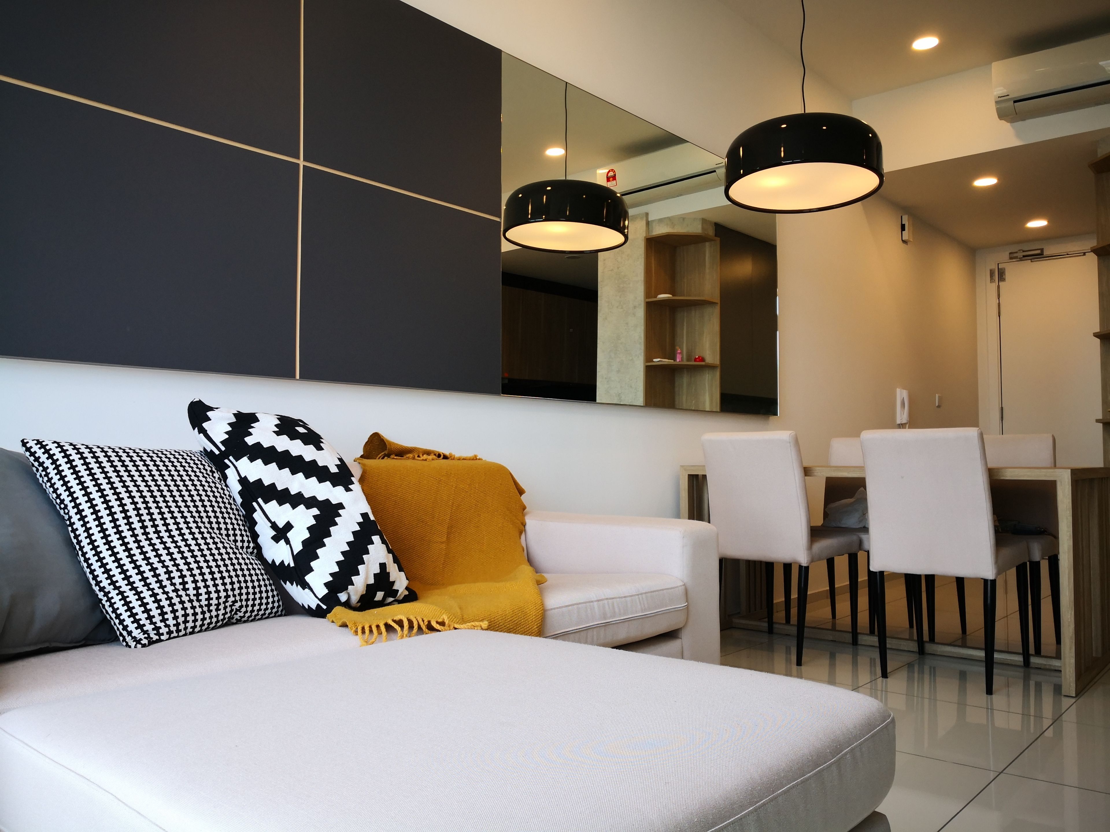 A modern living room with a white sofa, black and white patterned pillows, and a mustard-colored throw. There are two pendant lights above the sofa.