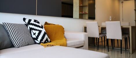A modern living room with a white sofa, black and white patterned pillows, and a mustard-colored throw. There are two pendant lights above the sofa.