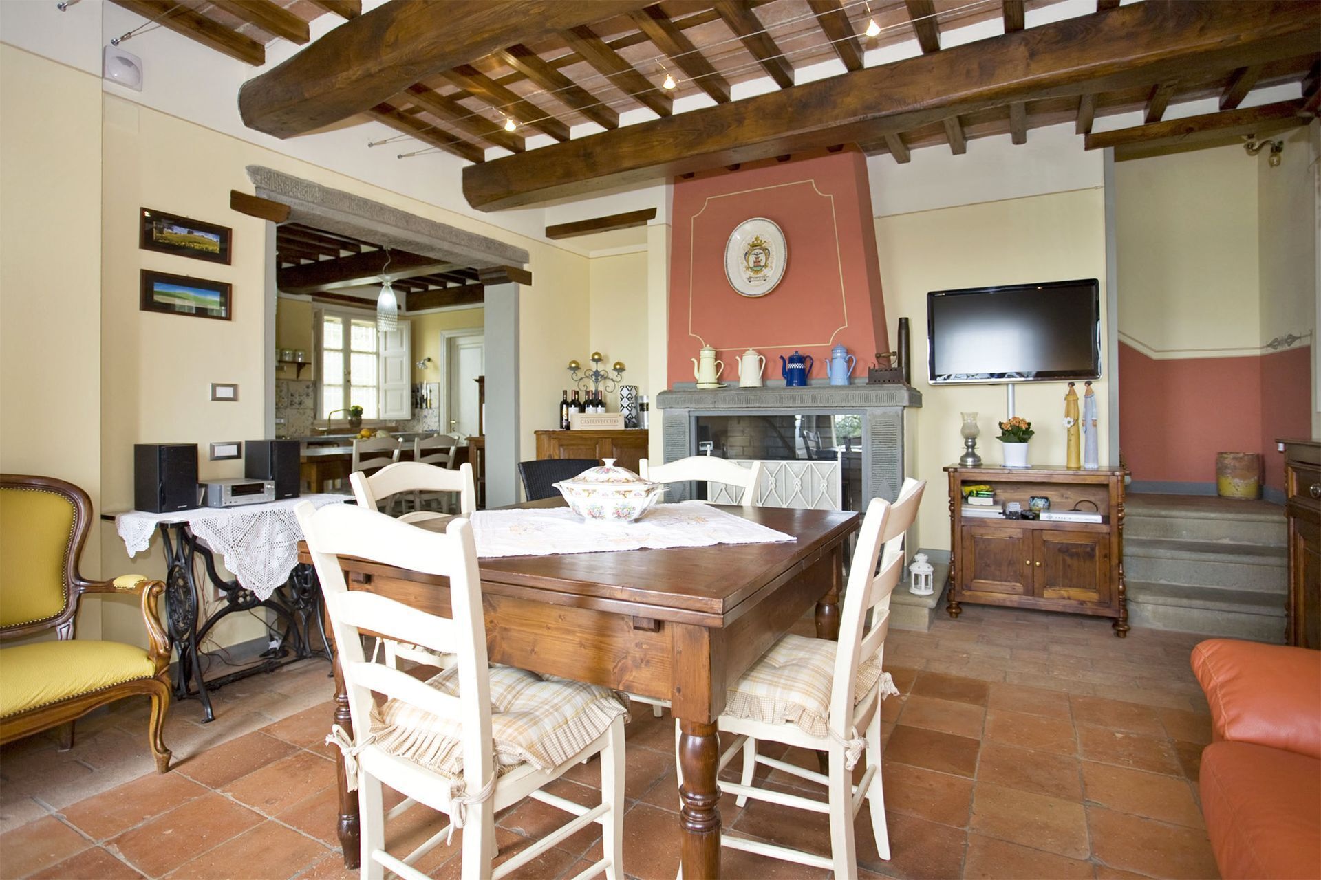A dining area with a wooden table and chairs, a fireplace, a television, and a kitchen in the background.