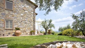 A stone building with a garden in front, including a pergola and potted plants.
