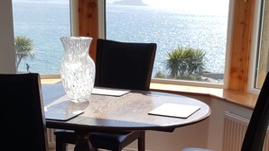 Una mesa de comedor con un florero y un bloc de notas, con vistas a un paisaje marino a través de amplias ventanas.
