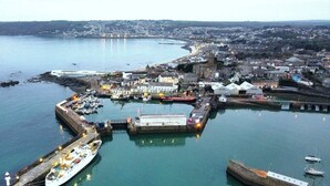 Vista aérea de un pueblo costero con un puerto deportivo, edificios portuarios y una iglesia destacada.