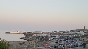 Un pueblo costero con un puerto deportivo, coches aparcados y una imponente torre de iglesia.