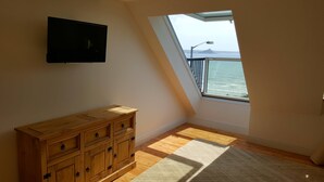 Una habitación con un aparador de madera, un televisor en la pared y un amplio ventanal con vistas al mar.