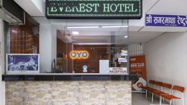 Een hotel receptie met een stenen muur, een neonbord voor Everest Hotel, en een bordje om de OYO app te downloaden.