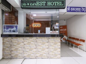 Zona de recepción de un hotel con pared de piedra, un letrero de neón del Hotel Everest y un anuncio para descargar la aplicación OYO.