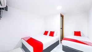 Een hotelkamer met twee bedden, elk voorzien van witte beddengoed en rode accenten, een klein nachtkastje en een witte airconditioningunit aan de muur.