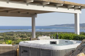 Un bain à remous installé sous une pergola, avec vue sur la mer et les collines.