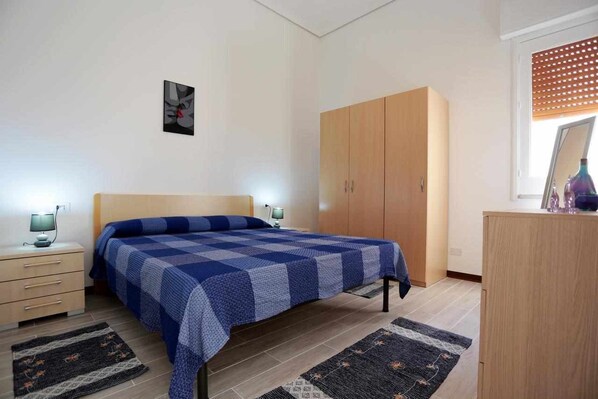 A bedroom with a bed, a wardrobe, a desk, and a nightstand.