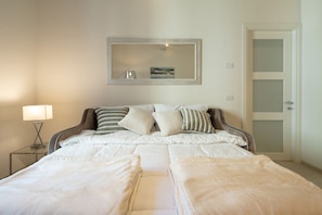 A bedroom with a bed, pillows, a bedside lamp, a mirror, and a door.