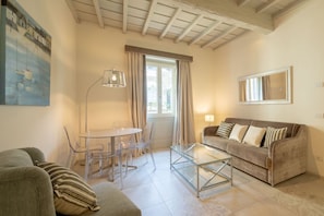 A living room with a sofa, a glass coffee table, a dining table with chairs, a lamp, and a window with curtains.
