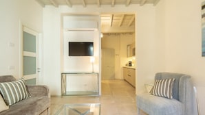 A living room with a sofa, armchair, glass coffee table, TV, and a kitchen in the background. - Carapelli 4 Fabulous apartment for up to four guests (florence)
