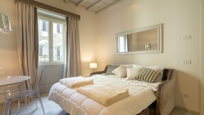 A bedroom with a bed, a bedside table, a chair, a window with curtains, and a mirror on the wall. - Carapelli 4 Fabulous apartment for up to four guests (florence)
