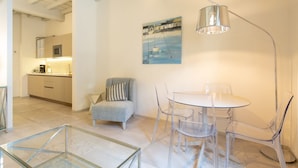 A modern kitchen with a microwave, a dining area with a round table and clear chairs, a gray armchair with a striped pillow, and a painting of boats on the wall. - Carapelli 4 Fabulous apartment for up to four guests (florence)