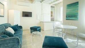 Un salon moderne comprenant un canapé, des poufs, un téléviseur et un coin repas avec une table et des chaises.