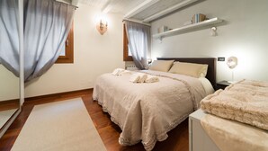 Une chambre à coucher avec un grand lit, une table de chevet, une commode, une étagère remplie de livres et une fenêtre avec des rideaux.