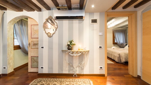 Une chambre d’hôtel avec un plafond en bois, un miroir décoratif, une petite table avec un vase et un tapis à motifs.