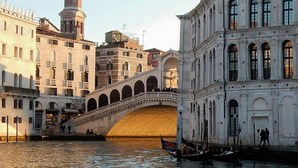 Un pont historique surmonté d’un dôme et d’un clocher, un canal où circulent des gondoles, et des bâtiments aux alentours qui présentent une architecture classique.