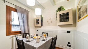 Un coin repas avec une table mise pour le petit-déjeuner, comprenant des assiettes, des tasses et un pichet. On y trouve également des placards fixés au mur, contenant de la verrerie, et un tableau encadré.