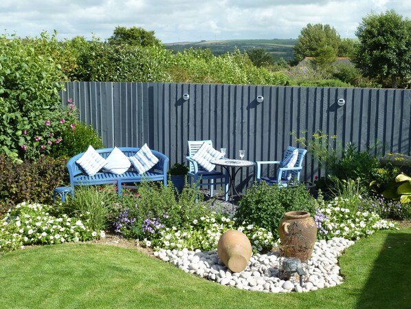 Un jardin doté d’un espace de détente extérieur bleu, comprenant un canapé et des fauteuils, et entouré d’une variété de plantes et de fleurs.