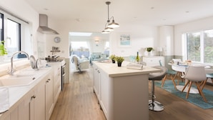 Een moderne keuken met een centraal eiland, een eethoek met een tafel en stoelen, en een uitzicht op de woonkamer op de achtergrond.