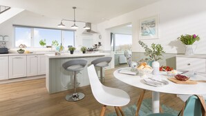 Een moderne keuken met witte kasten, een centraal keukenblok met barkrukken, en een eettafel gedekt voor vier personen.