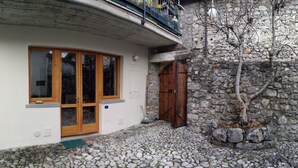 A stone building with a wooden door and windows, a stone wall, and a tree in front. - Lake Iseo in Esmate:The House of Fairies CIR.016200CNI00013 CIN IT016200C2UAHS6HFE (Solto Collina)